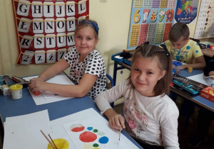 Sala lekcyjna, uśmiechnięte dziewczynki malują farbami kropkowe dzieła sztuki