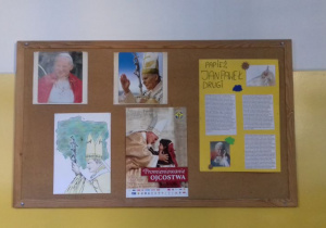 Tablica przedstawiająca plakaty, zdjęcia i prace plastyczne uczniów z papieżem Janem Pawłem II.