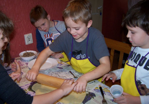 Pięcioro uczniów stoi przy stole, uśmiechnięty chłopiec wałkuje ciasto na pierogi.