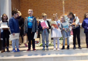 Dzieci w rzędzie na schodach kościoła z dyplomami i nagrodami w rękach.