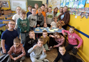 Sala lekcyjna, zgromadzeni przy stoliku uczniowie poznają produkty zbożowe.