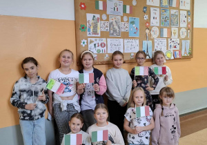 Korytarz szkolny, uśmiechnięci chłopcy prezentują samodzielnie wykonane flagi Włoch oraz tablicę z symbolami Italii.