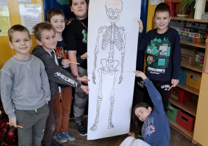 Sala lekcyjna, uczniowie prezentują wykonany podczas pracy w grupie szkielet człowieka.