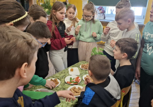 Sala lekcyjna, zadowoleni uczniowie zgromadzeni wokół stołu degustują włoskie przysmaki