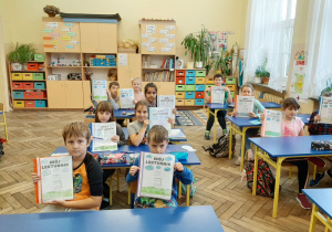 Sala lekcyjna, uśmiechnięci siedzący w ławkach uczniowie prezentują wykonane samodzielnie "Lekturniki".